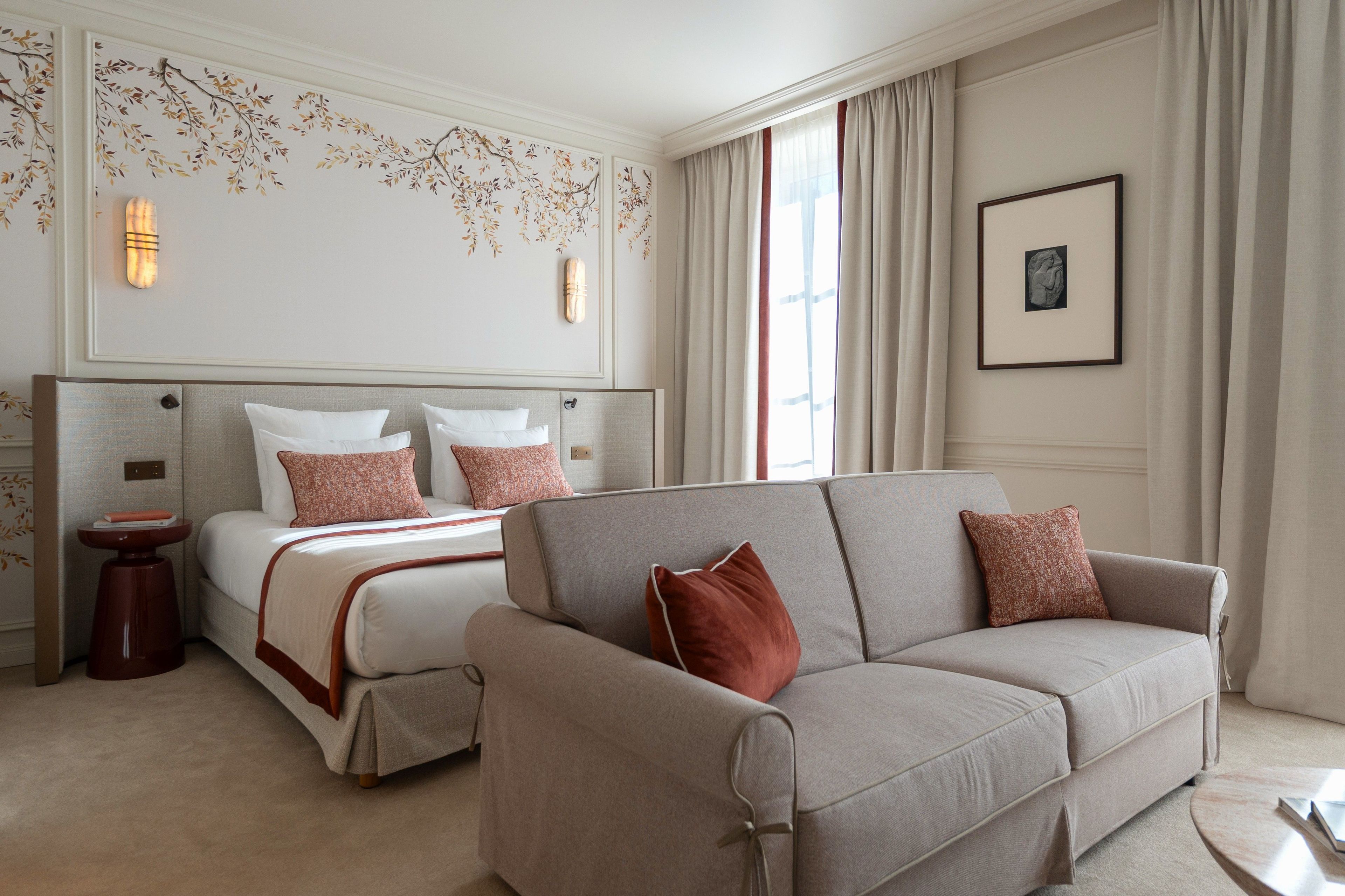 A hotel room with a bed, a sofa, a small table, and a wall with decorative elements.