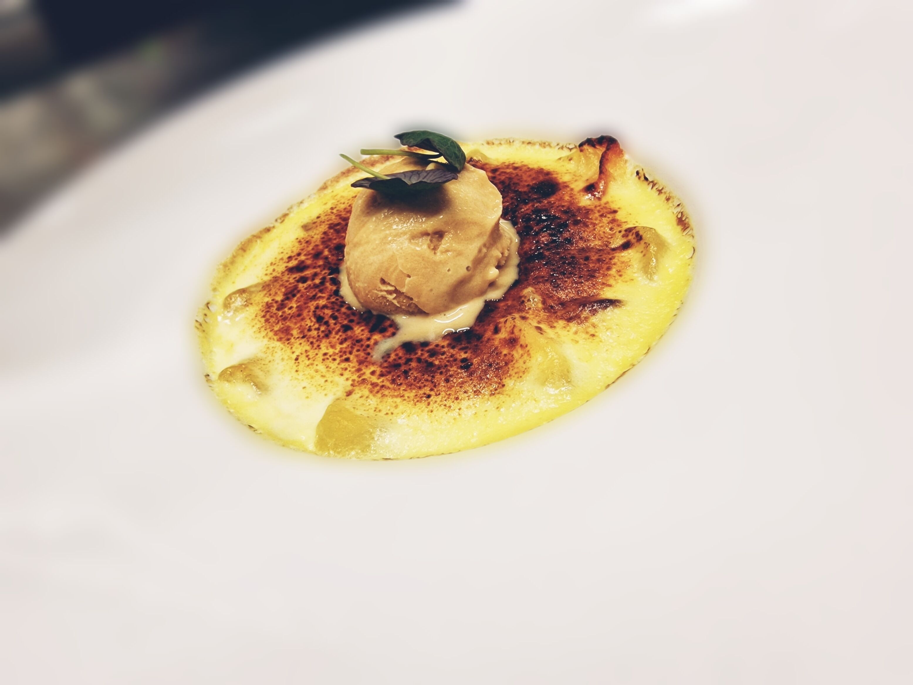 Un dessert servi dans une assiette blanche, agrémenté d’une quenelle de crème et d’une feuille de menthe.
