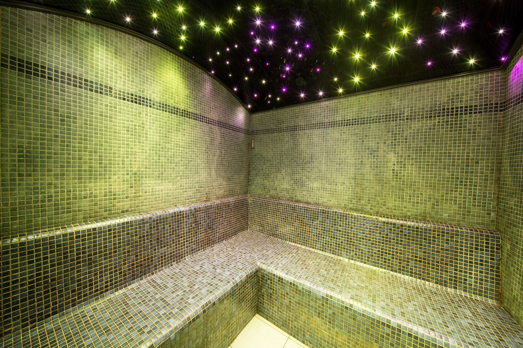 A tiled room with a bench and a ceiling with star-like lights.