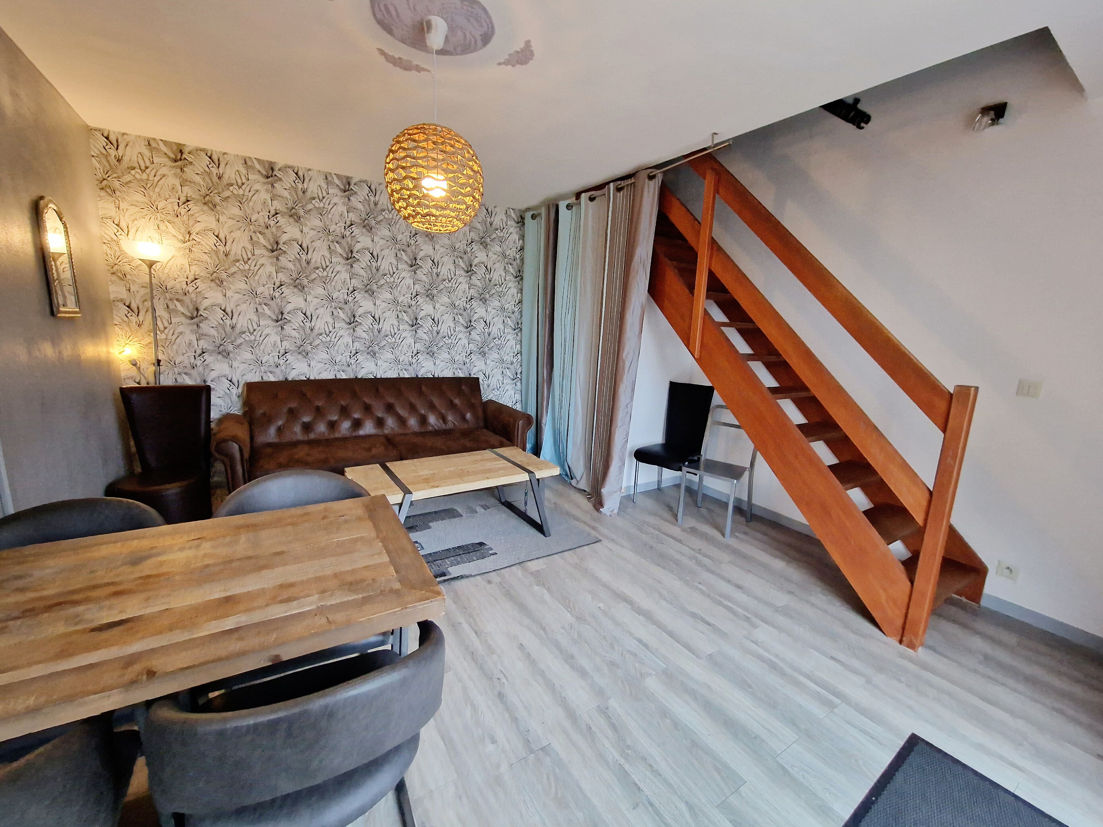 Una sala de estar moderna con un sofá de cuero marrón, una mesa de centro de madera y una escalera con barandillas de madera.