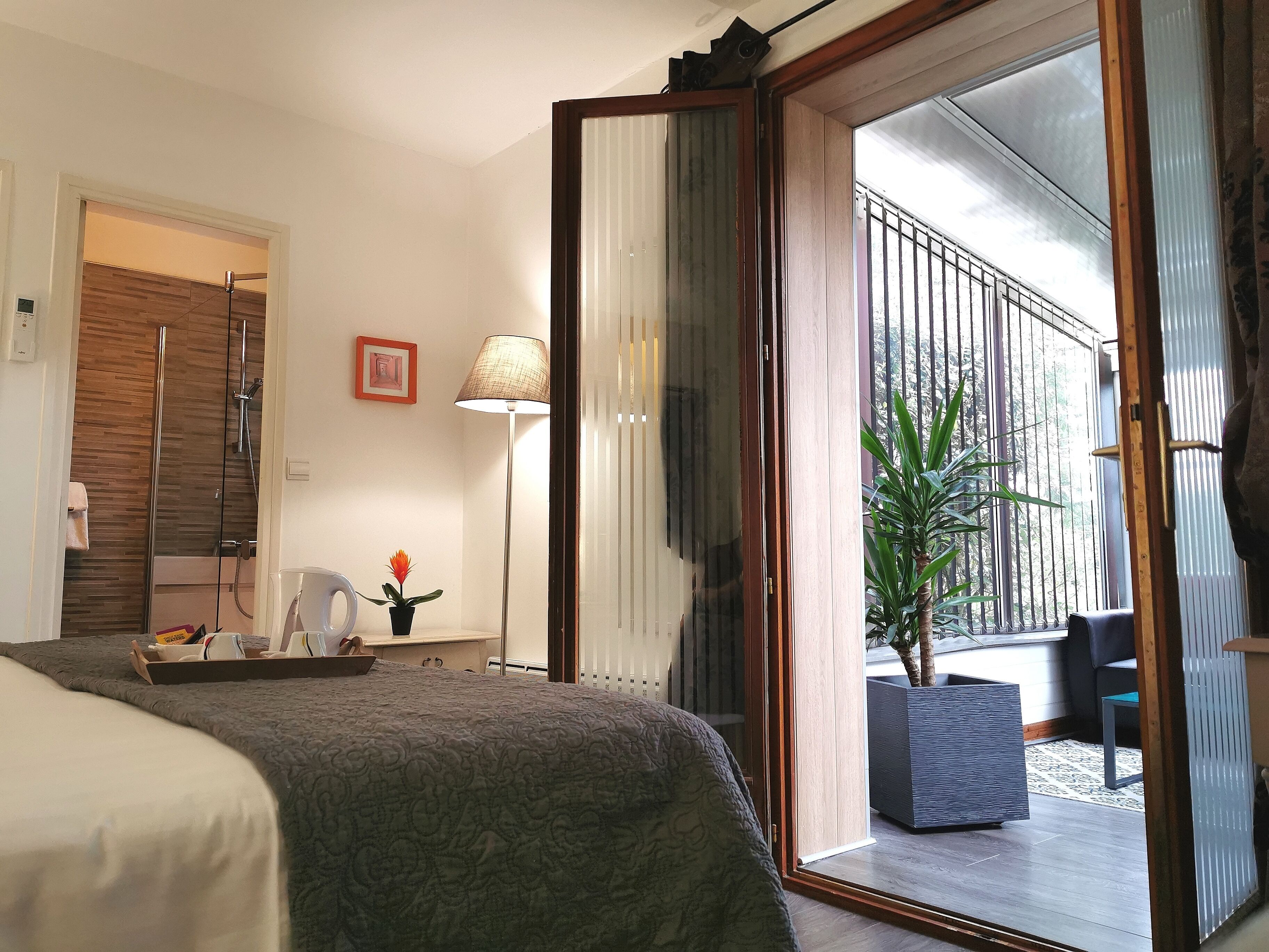 A hotel room with a bed, a desk, a lamp, and a view of the outside balcony.