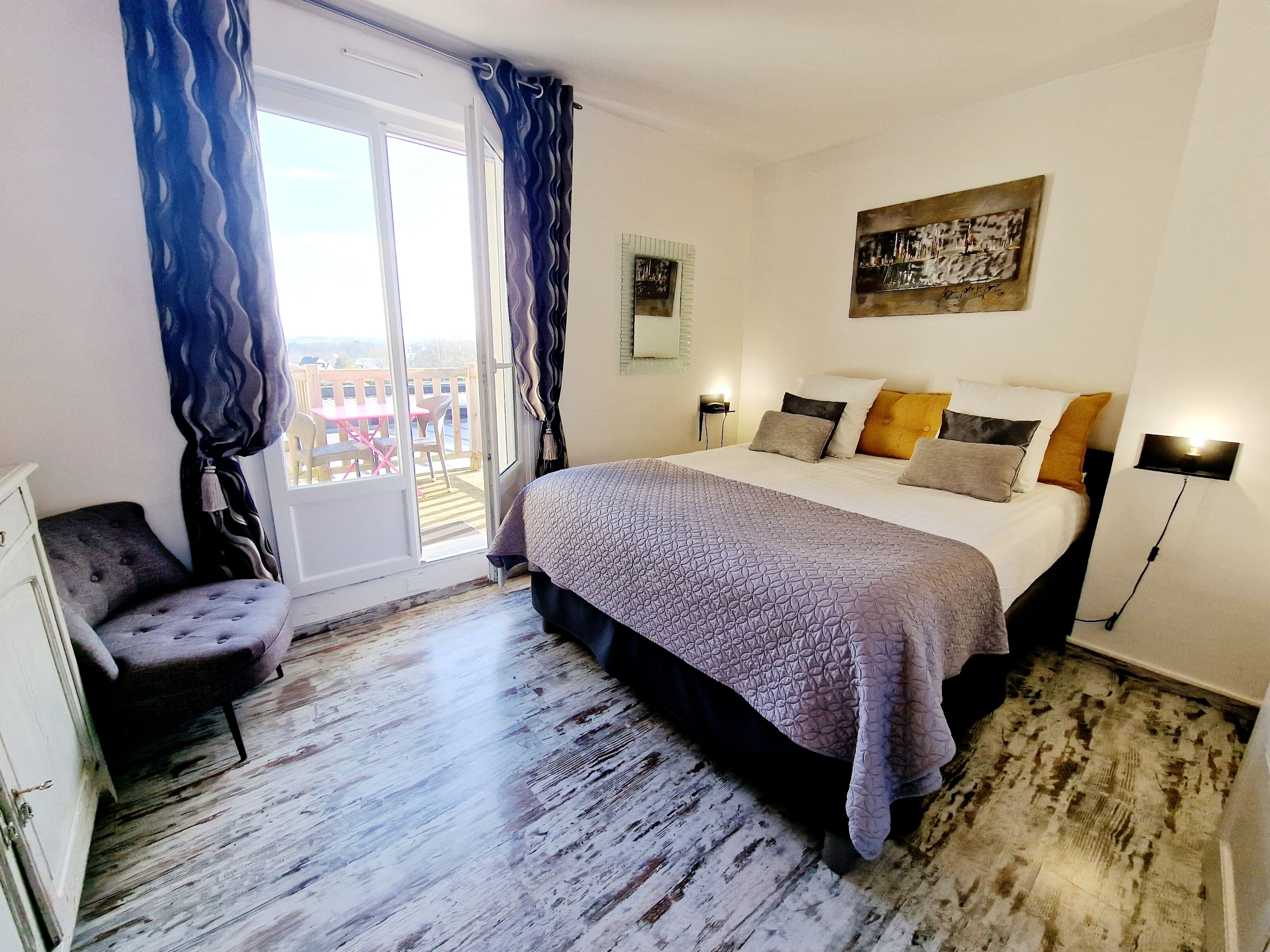 Un dormitorio con cama, una silla, un cuadro y vistas a través de una ventana.
