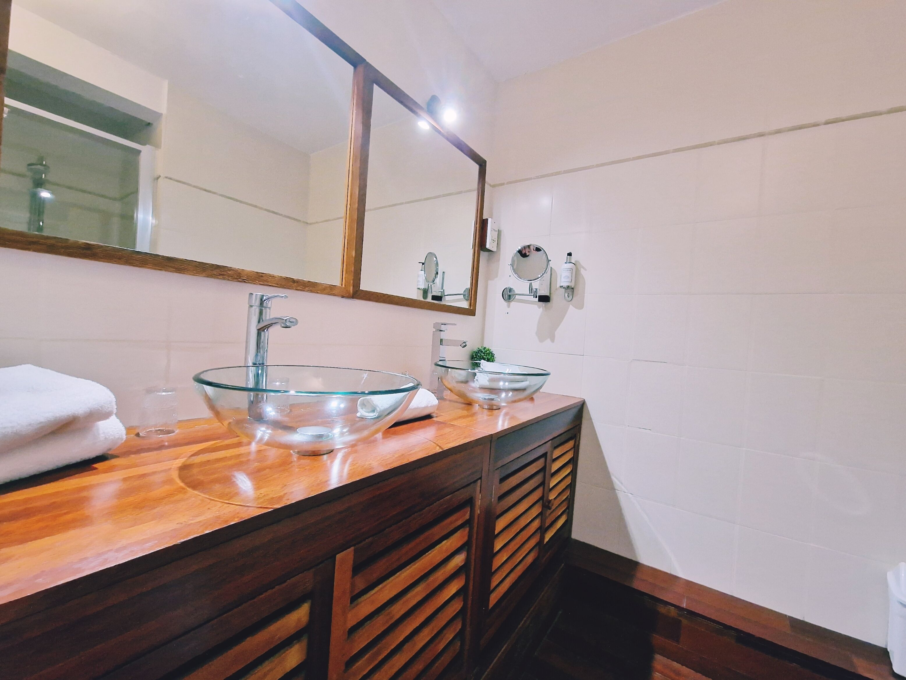 A bathroom with two glass bowl sinks, wooden vanity, and a large mirror.