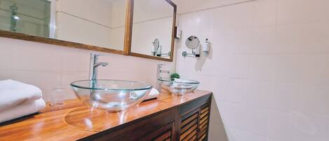 A bathroom with two glass bowl sinks, wooden vanity, and a large mirror.