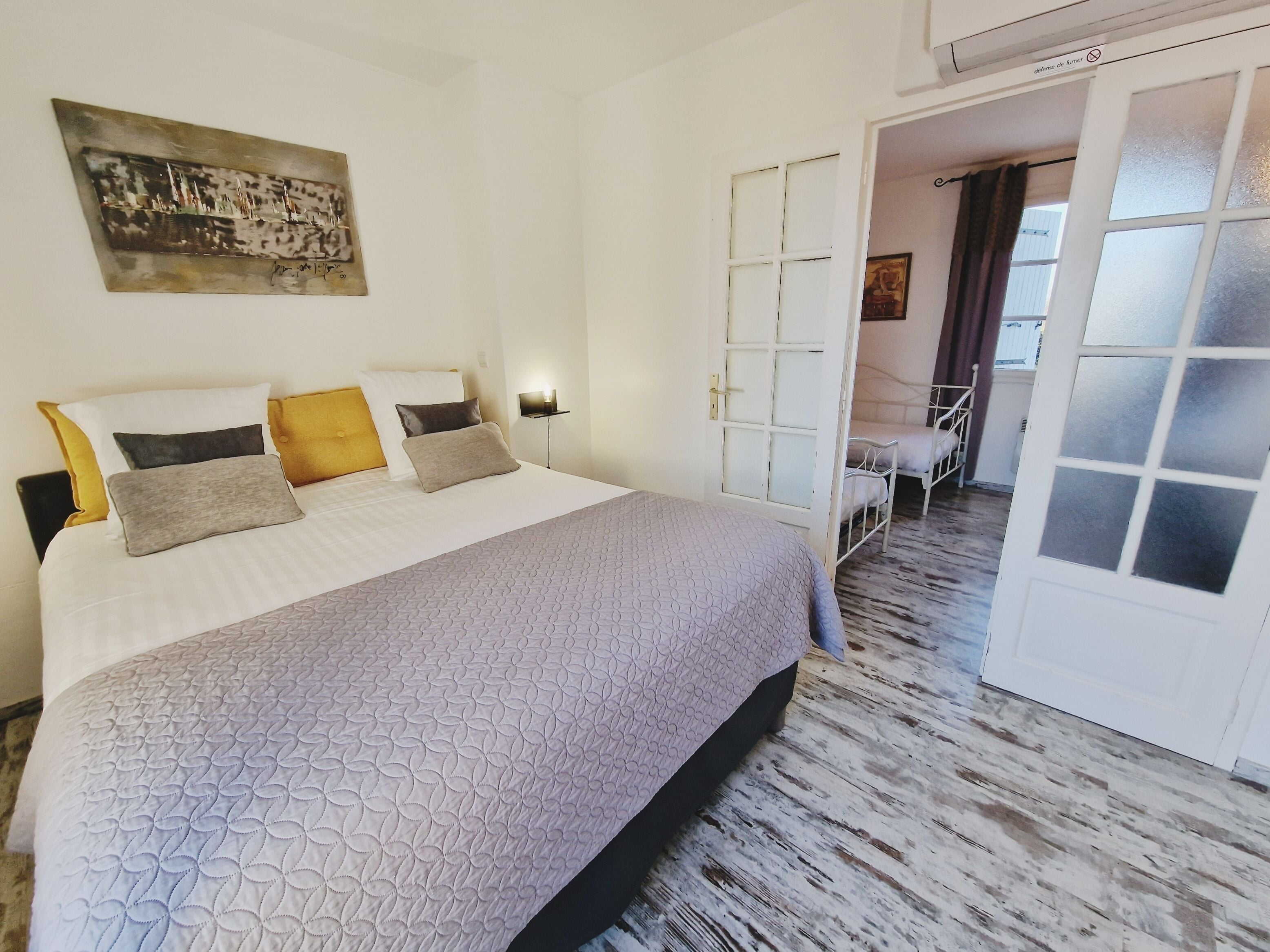 Een netjes opgemaakt bed met een beddegoed met een patroon, een nachtkastje met een lamp en een schilderij aan de muur.