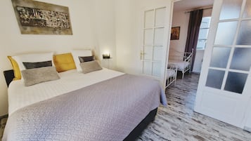 Een netjes opgemaakt bed met een beddegoed met een patroon, een nachtkastje met een lamp en een schilderij aan de muur.