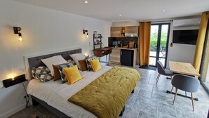 Un dormitorio moderno con una cama grande, mesitas de noche, un escritorio empotrado y una pequeña kitchenette.