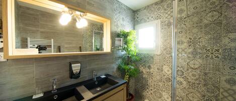 Un baño moderno con lavamanos doble, un espejo grande, una ducha y azulejos estampados.