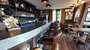 Zona de bar con una barra alargada, taburetes y una exhibición de botellas y vasos.