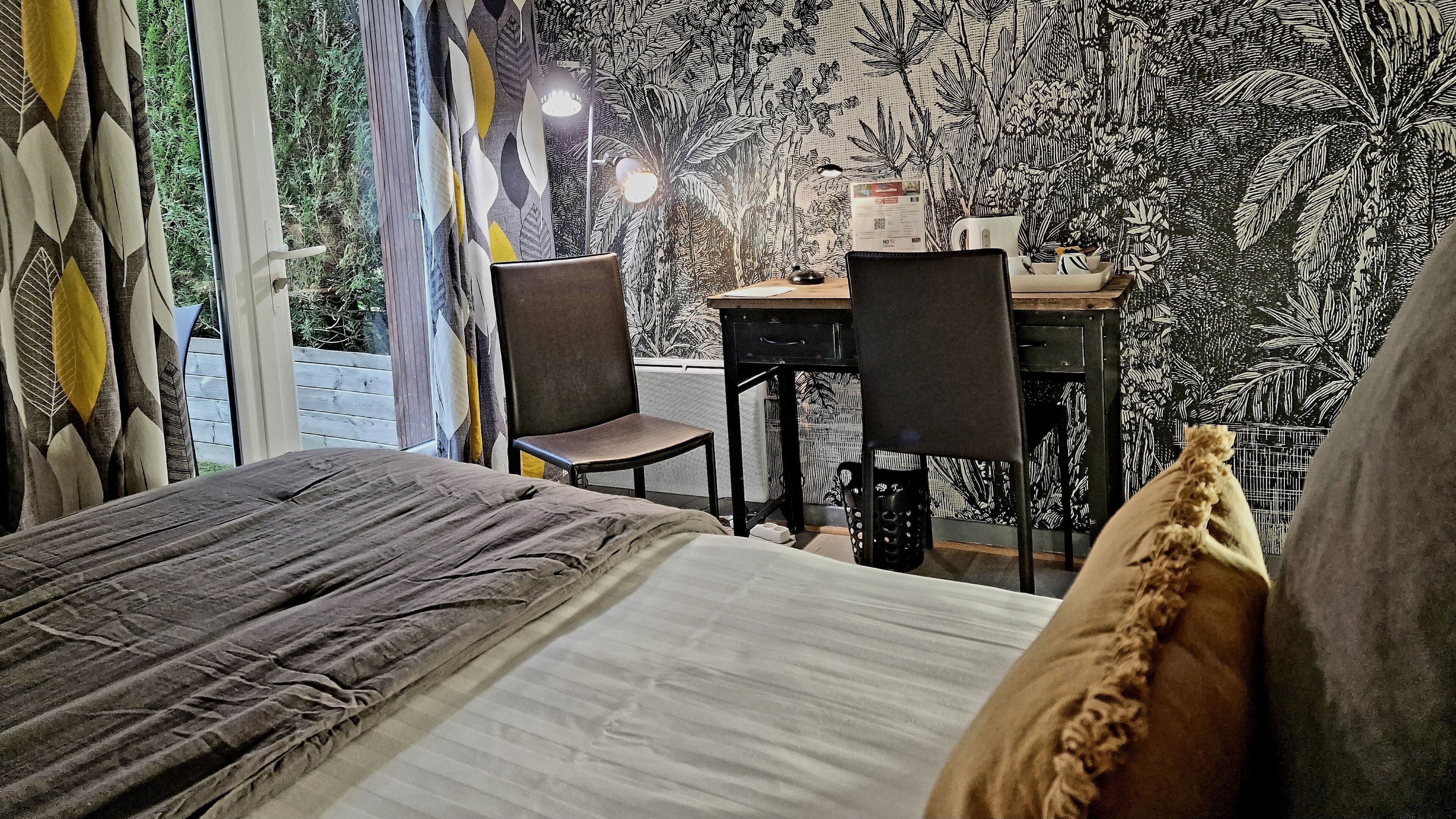 A bedroom with a bed, a desk, two chairs, and a window with curtains.