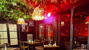 Un restaurante con mesas y sillas de madera, lámparas colgantes y vistas a la ciudad a través de amplios ventanales.