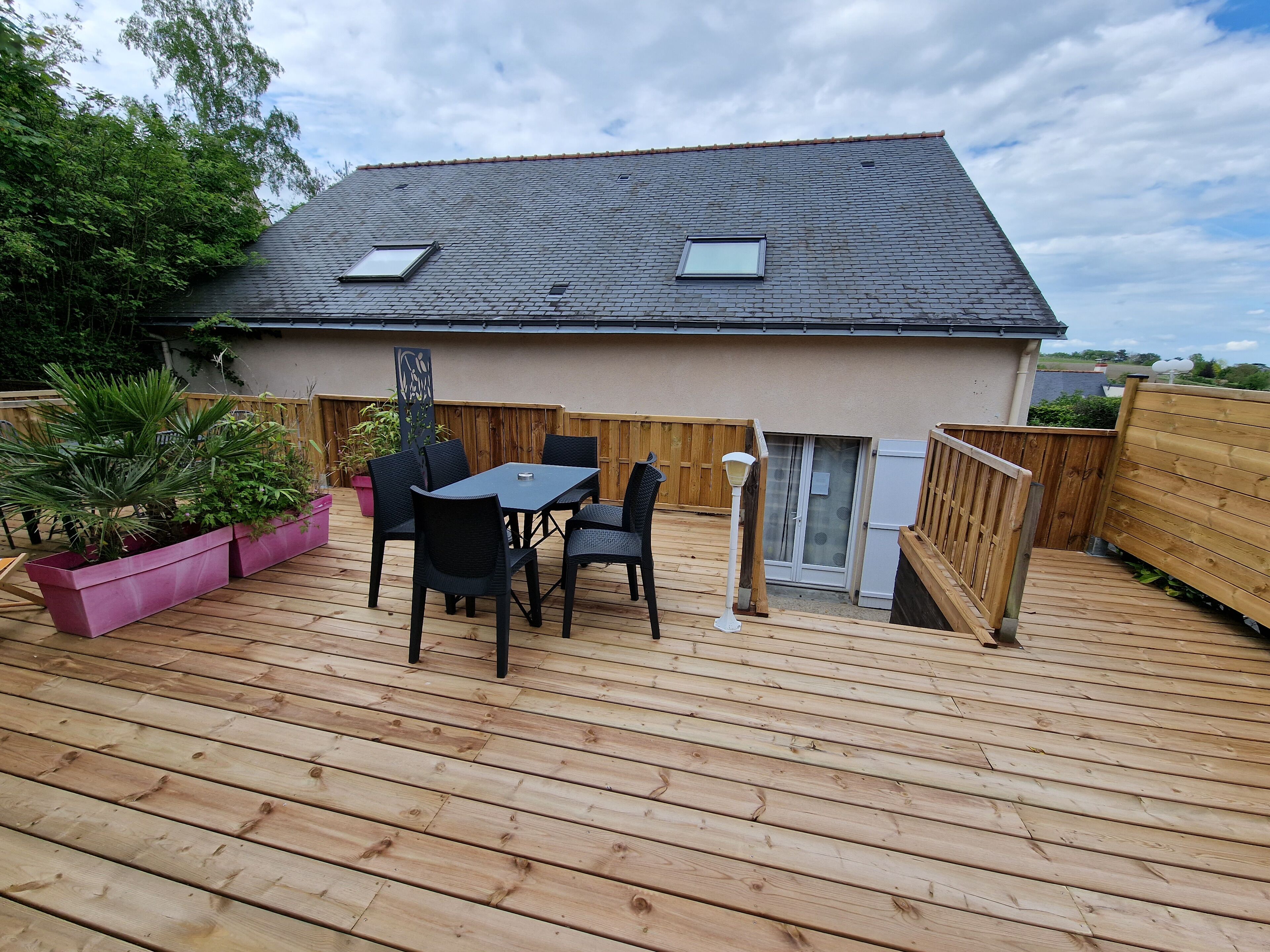 A wooden deck with a table and chairs, a potted plant, and a wooden fence.
