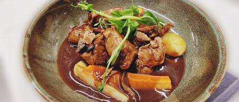 Un plato de cerámica con estofado de carne, papas y verduras, adornado con vegetales verdes.