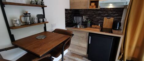 Une cuisine de taille réduite, avec des meubles de rangement en bois, un réfrigérateur noir et une machine à café posée sur le plan de travail.