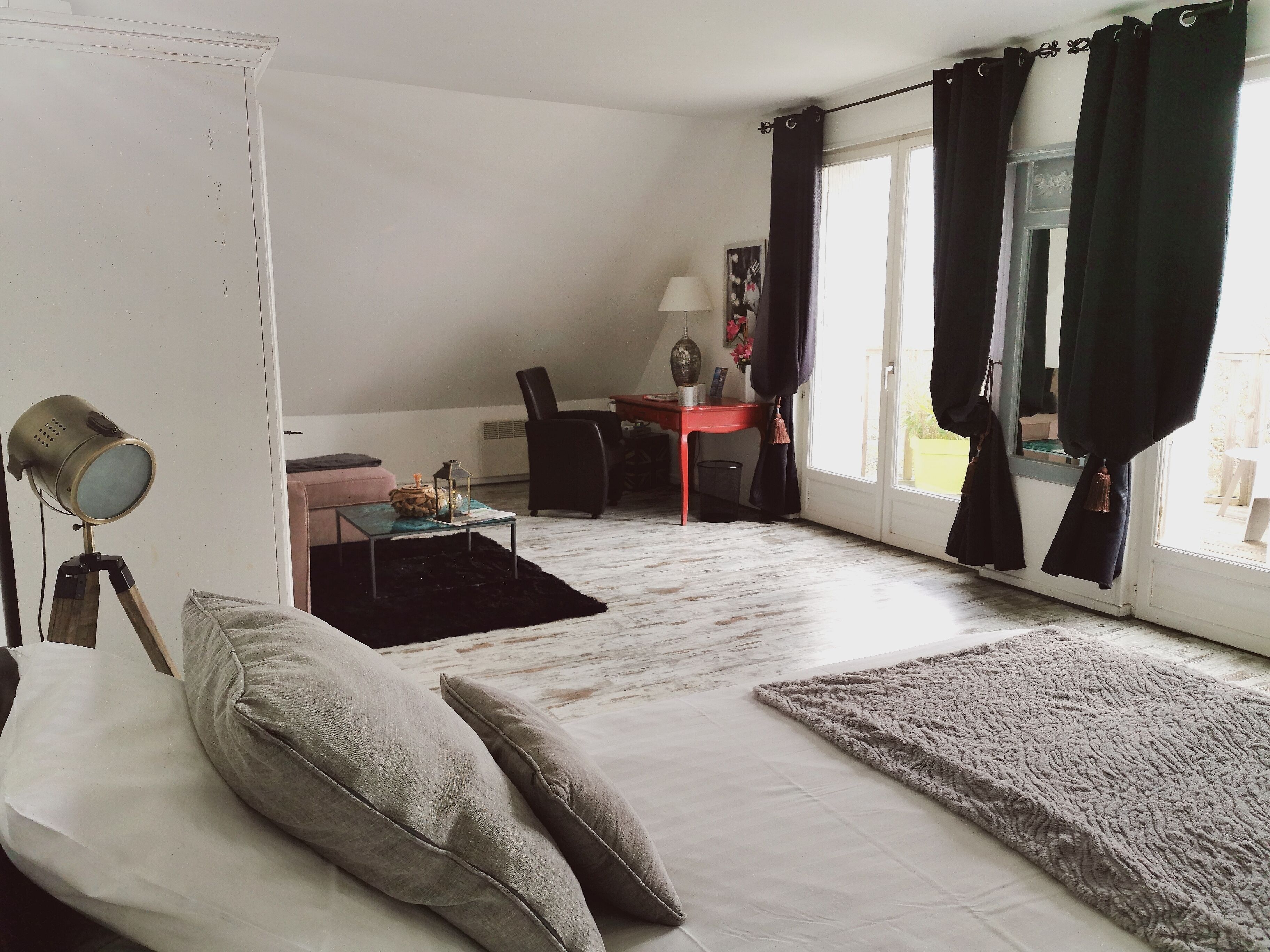 Una sala de estar con un sofá, una mesita, una lámpara y una silla. Hay una ventana con cortinas y vistas al exterior.