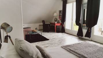 Una sala de estar con un sofá, una mesita, una lámpara y una silla. Hay una ventana con cortinas y vistas al exterior.