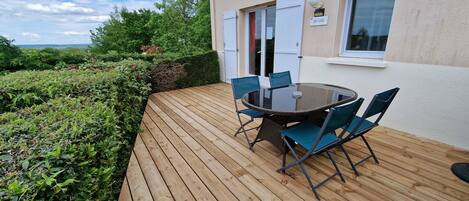 A wooden deck with a glass table and chairs, a door, and a window with a sign.