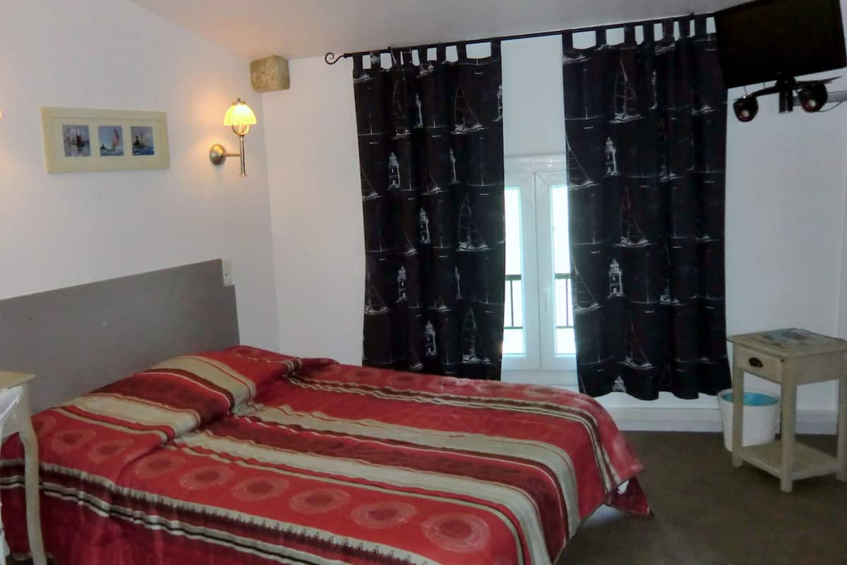Ein Zimmer mit einem Bett, zwei Wandlampen, einem Schreibtisch mit Stuhl, einem kleinen Tisch und einem Fenster mit Vorhängen.
