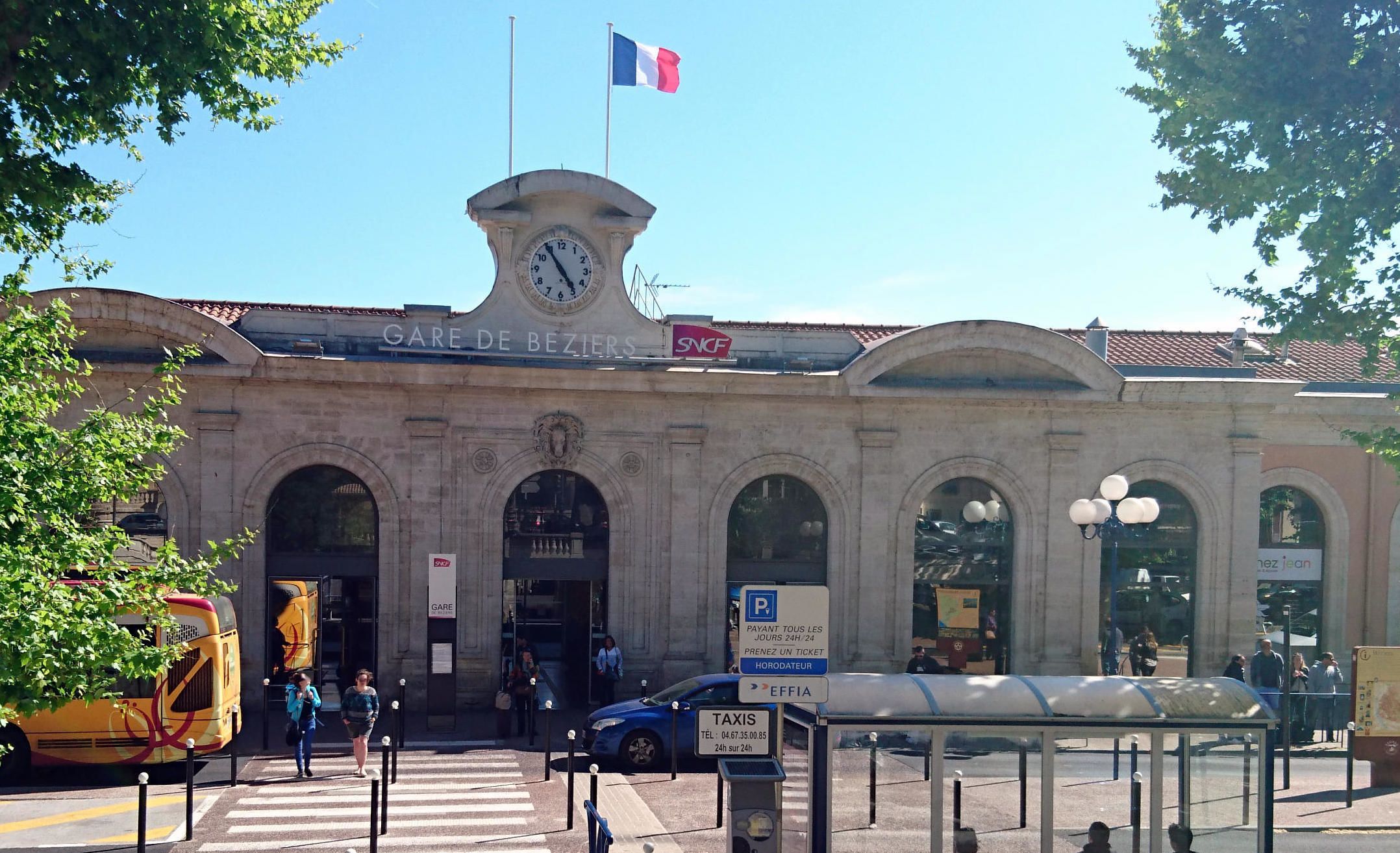 A building with a clock tower, a sign for Gare de Beziers, and a taxi stand.