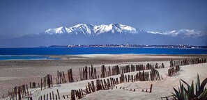 A coastal landscape with a snow-capped mountain in the background, a sandy beach in the foreground, and a wooden fence. - Citotel Las Cigalas (Villeneuve-les-Beziers)