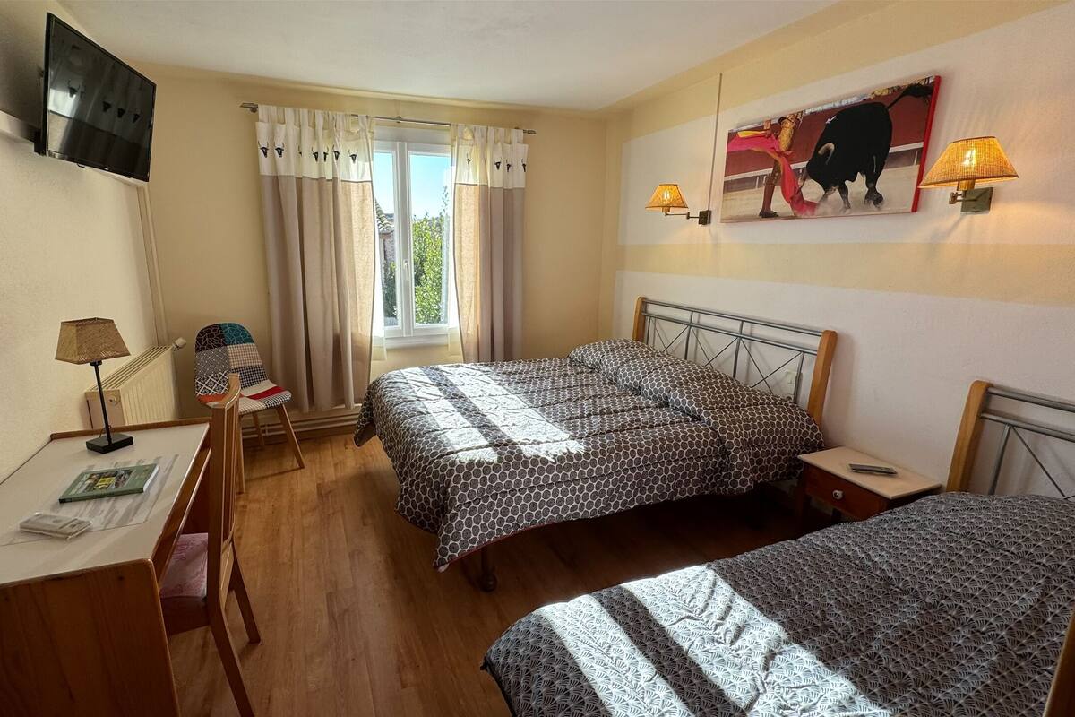 Ein Hotelzimmer mit zwei Betten, einem Schreibtisch, einem Sessel, einem Fernseher und einem Fenster mit Vorhängen.