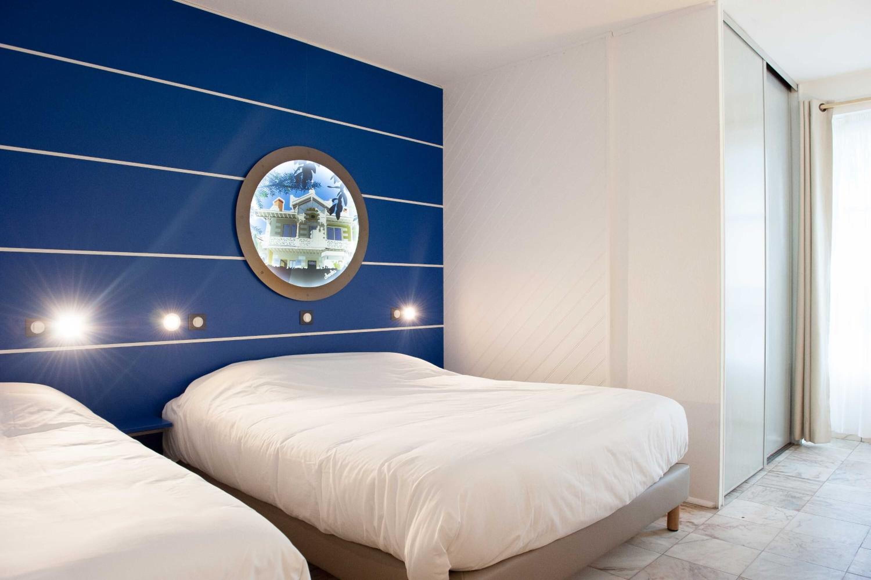 A hotel room with two beds, a large mirror, and a view of a building through the mirror.