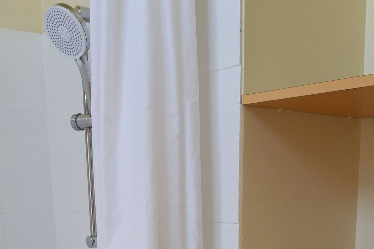 Een badkamer met een douche, een handdoekhouder en een zeepdispenser.