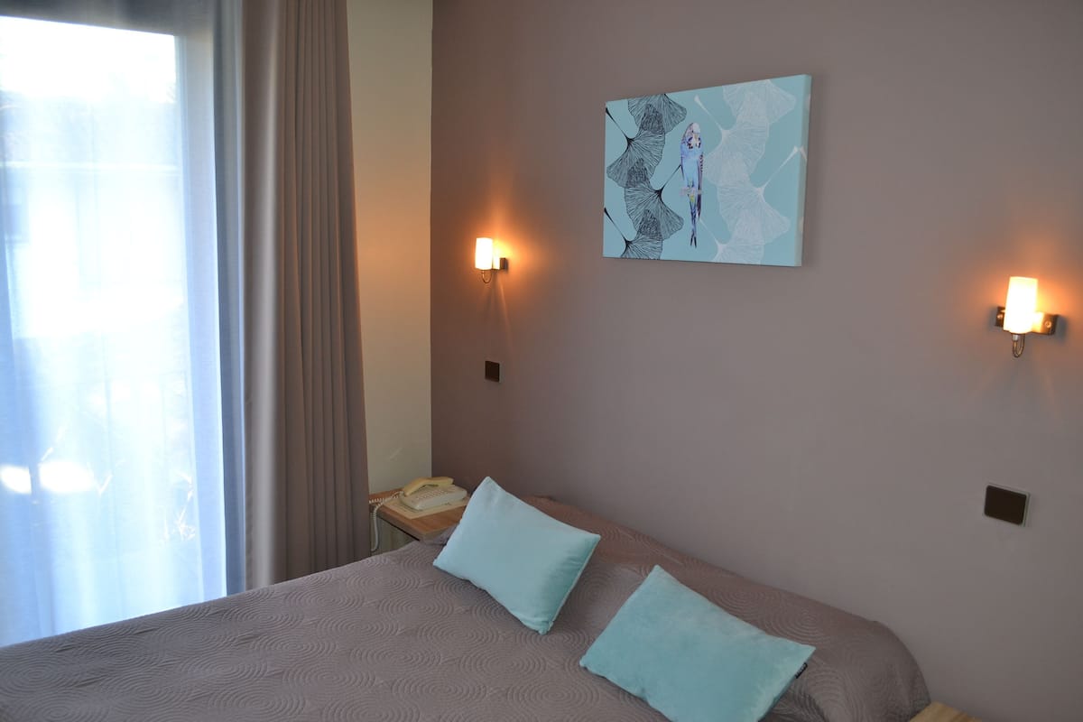 Hotelkamer met een bed, twee kussens, een nachtkastje met telefoon en wandlampen.
