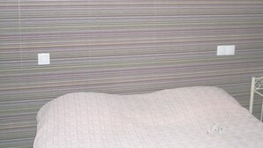 A room with a bed, a metal stand with a bag, and a striped wall. - Cit'Hotel Saint Jacques  (Blois)