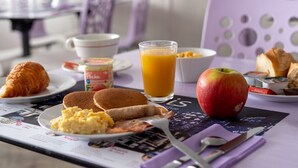 A breakfast setting with croissants, pancakes, scrambled eggs, bacon, an apple, orange juice, and yogurt on a table with a menu. - Cit'Hotel Saint Jacques  (Blois)