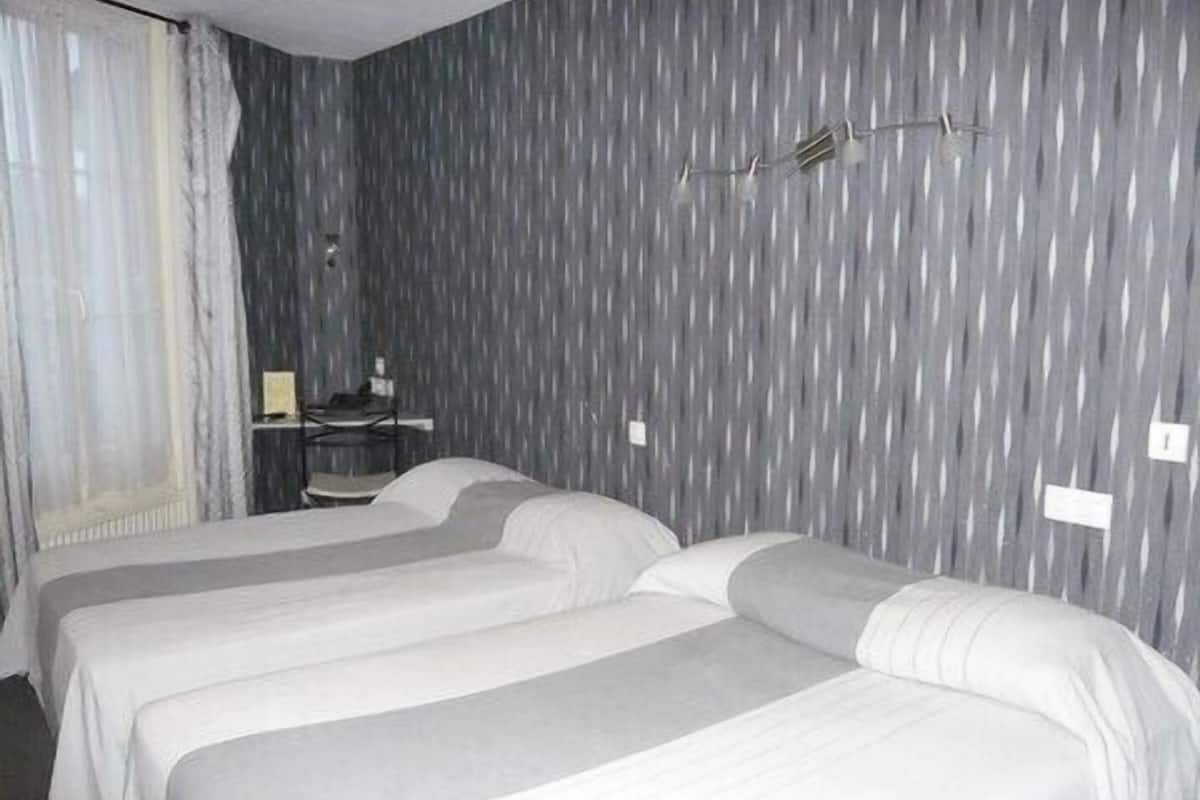 A hotel room with two single beds, a desk, and a chair.