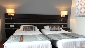 Habitación de hotel con dos camas, cada una con almohada y mesita de noche.