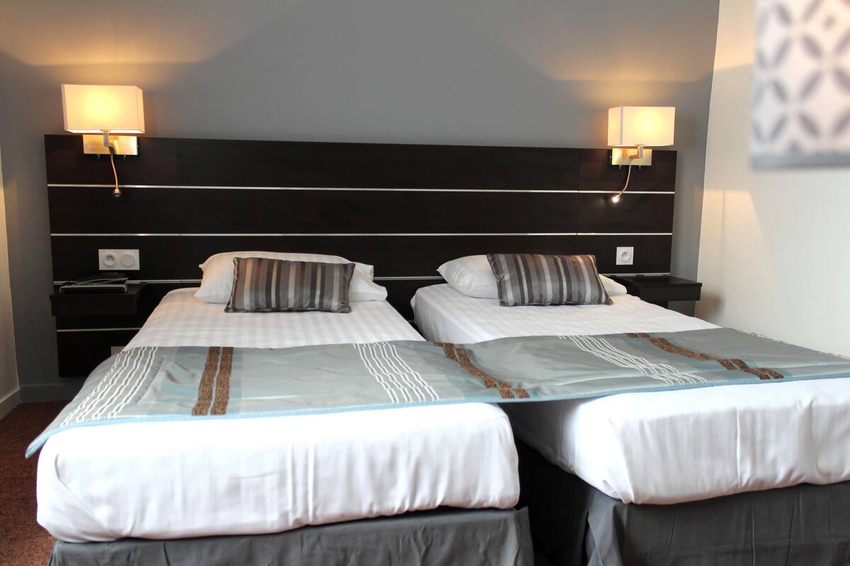 A hotel room with two beds, each with a pillow and a bedside table.