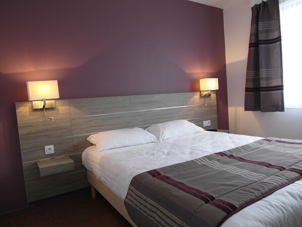 A hotel room with a bed, nightstands, and wall-mounted lamps.