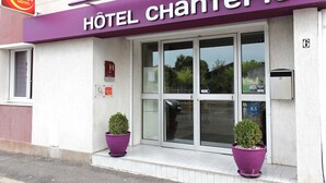 Entrada de hotel con toldo morado, dos plantas en macetas y un cartel de contacto.