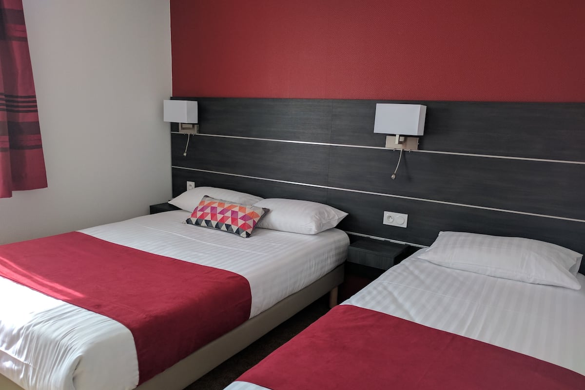 A hotel room with two beds, each with a red and white bedspread, a pillow with a geometric pattern, and a dark headboard.