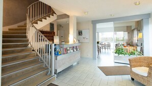 Un interior moderno con una escalera, un mostrador de recepción, un comedor y una sala de estar con un sofá de mimbre.
