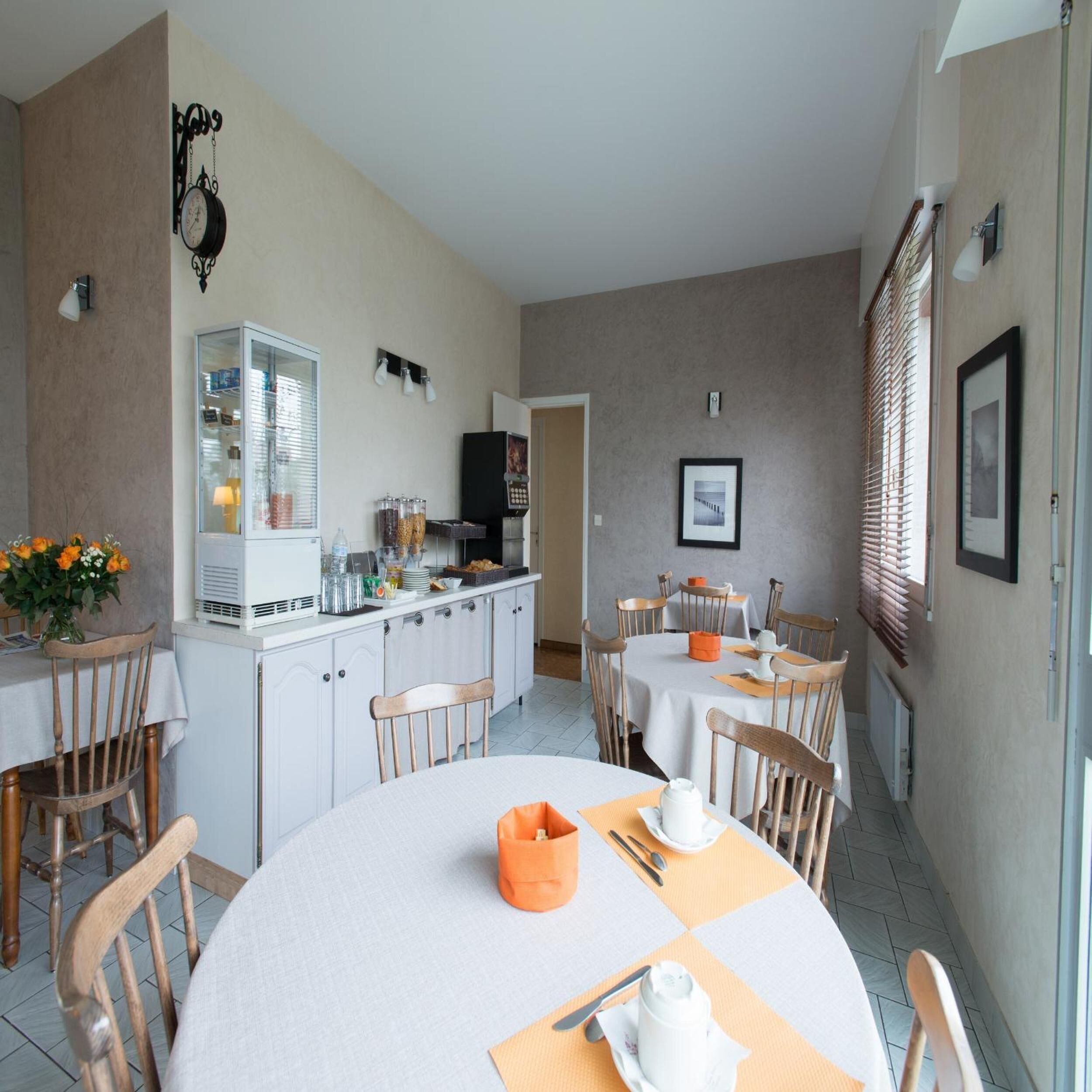 A dining area with round tables, wooden chairs, a white cabinet with a glass door, and a clock on the wall.