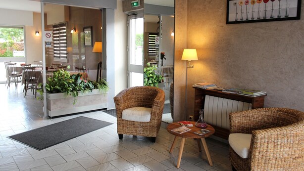 Un vestíbulo de hotel con muebles de mimbre, un mostrador de recepción, un espejo y un arreglo floral en la pared.