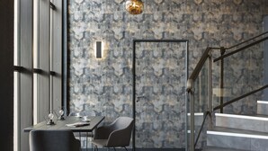A modern interior with a staircase, a dining area with chairs and a table, and a patterned wall.