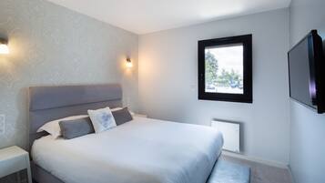 Un dormitorio moderno con una cama grande, mesitas de noche, un televisor montado en la pared y una ventana con vistas al exterior.