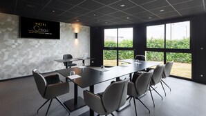 A modern hotel conference room with a large table, chairs, and a TV screen displaying the hotel name.