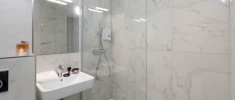 A modern bathroom with a glass-enclosed shower, a white sink, and marble tiles.