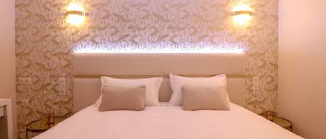 A neatly made bed with two pillows, a headboard with integrated lighting, and patterned wallpaper.