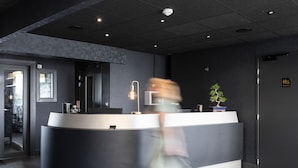 A modern reception desk with a dark color scheme, a potted plant, and a sign indicating the location of toilets.