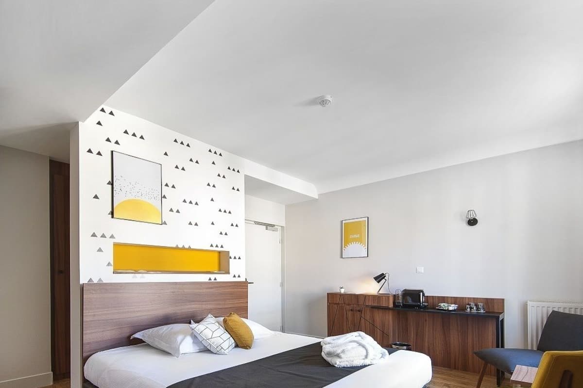 A modern hotel room with a large bed, a wooden desk, and a chair.