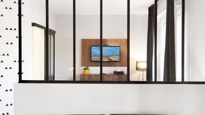 Una sala moderna con un sofá gris, un cojín amarillo y un televisor con marco negro sobre un soporte de madera.