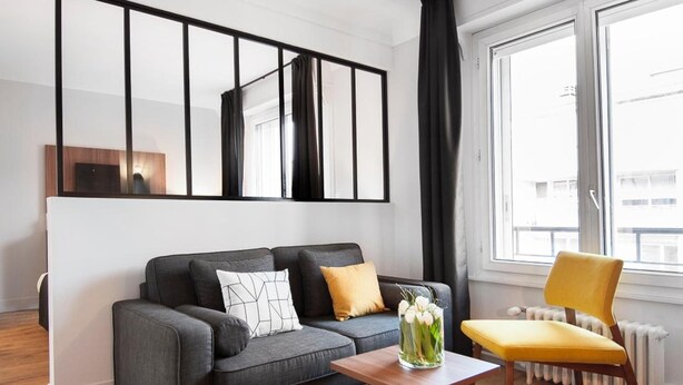 A modern living room with a grey sofa, a yellow armchair, a wooden coffee table, and a large window with curtains. - Hôtel Métropole (Boulogne-sur-Mer)