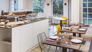 A modern kitchen with a central island, large windows, and a dining area with yellow chairs. - Hôtel Métropole (Boulogne-sur-Mer)