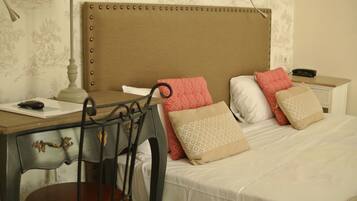 A hotel room with a wooden desk, a chair, a bed with patterned pillows, and a nightstand with a phone.